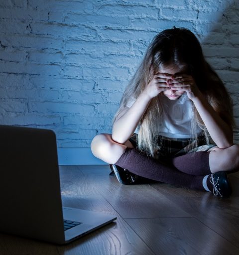 Scared sad girl bullied on line with laptop suffering cyberbullying and harassment feeling desperate and intimidated. Child victim of bullying stalker social media network